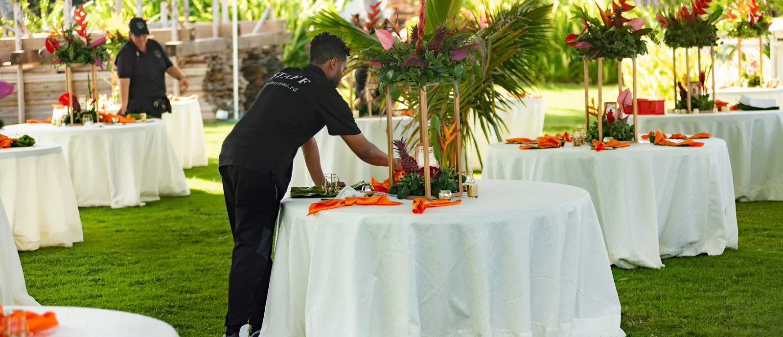 Staff setting reception tables with tropical centrepieces on a private lawn